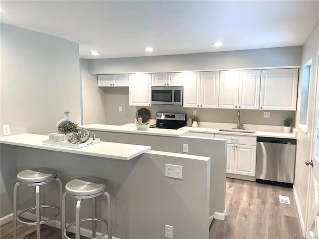 kitchen featuring appliances with stainless steel finishes, light wood-type flooring, a sink, white cabinets, and a breakfast bar