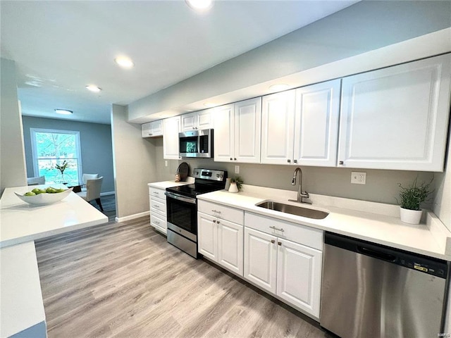 kitchen with light wood-type flooring, a sink, stainless steel appliances, recessed lighting, and white cabinetry
