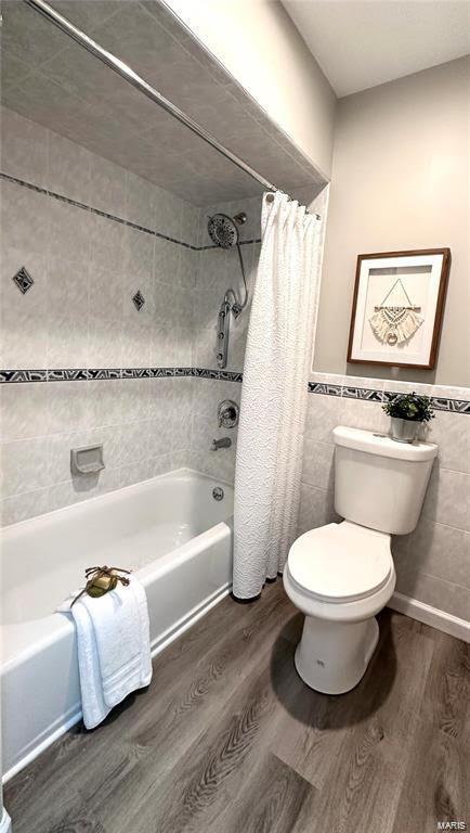 full bath with wainscoting, toilet, shower / bath combination with curtain, tile walls, and wood finished floors