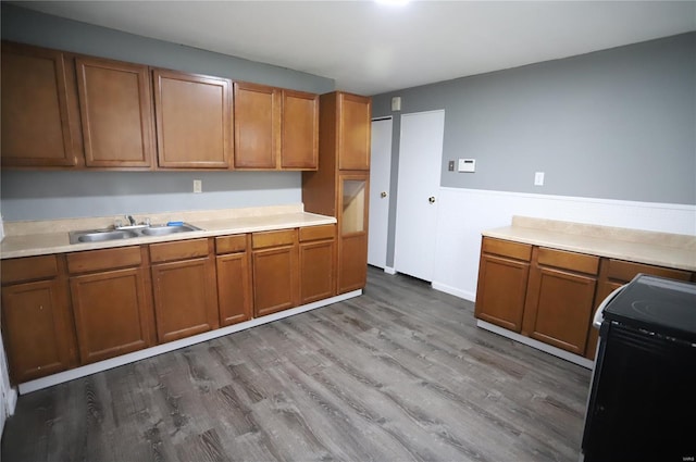 kitchen featuring wood finished floors, brown cabinetry, black electric range oven, and a sink
