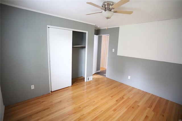 unfurnished bedroom with ornamental molding, a closet, a ceiling fan, and wood finished floors