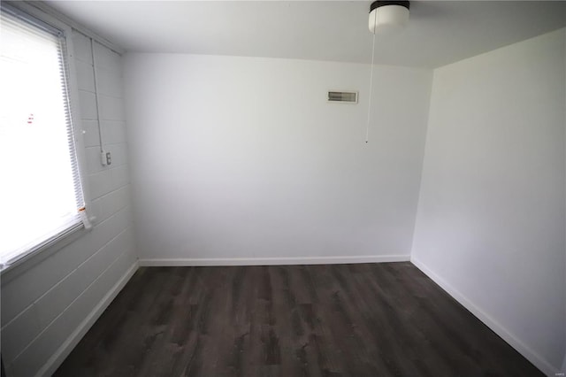 spare room with dark wood-style flooring, visible vents, and baseboards