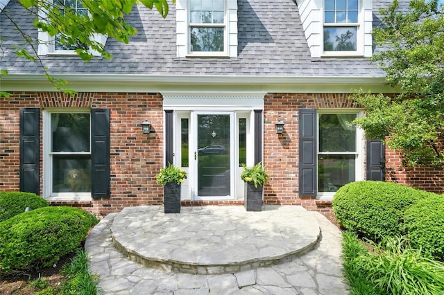 doorway to property featuring roof with shingles and brick siding