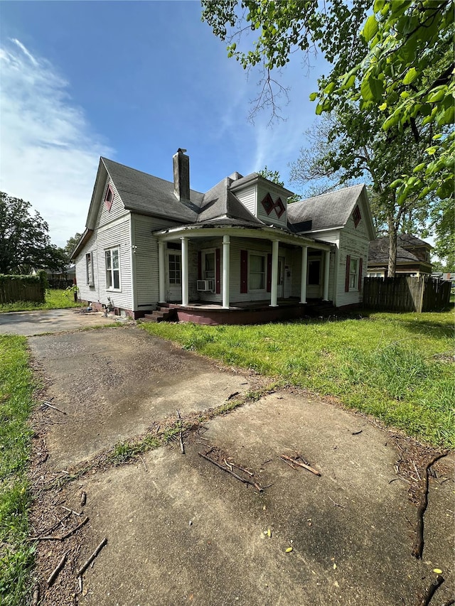 view of front of home with a chimney, covered porch, fence, cooling unit, and a front yard