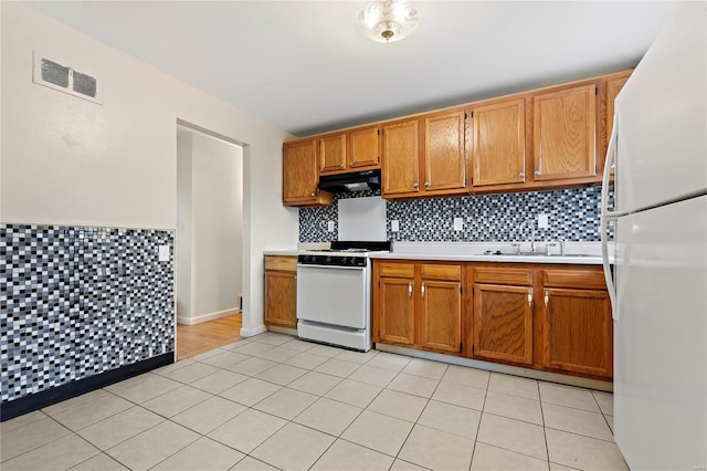 kitchen featuring white appliances, under cabinet range hood, light countertops, a sink, and visible vents