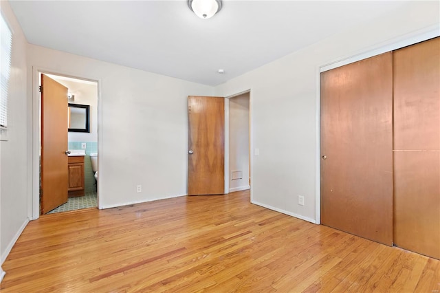 unfurnished bedroom with baseboards, light wood-style floors, connected bathroom, and a closet