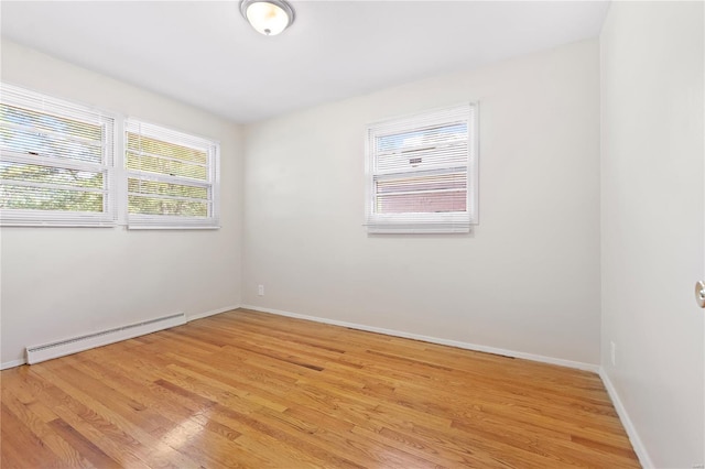 spare room with a baseboard heating unit, light wood finished floors, and baseboards