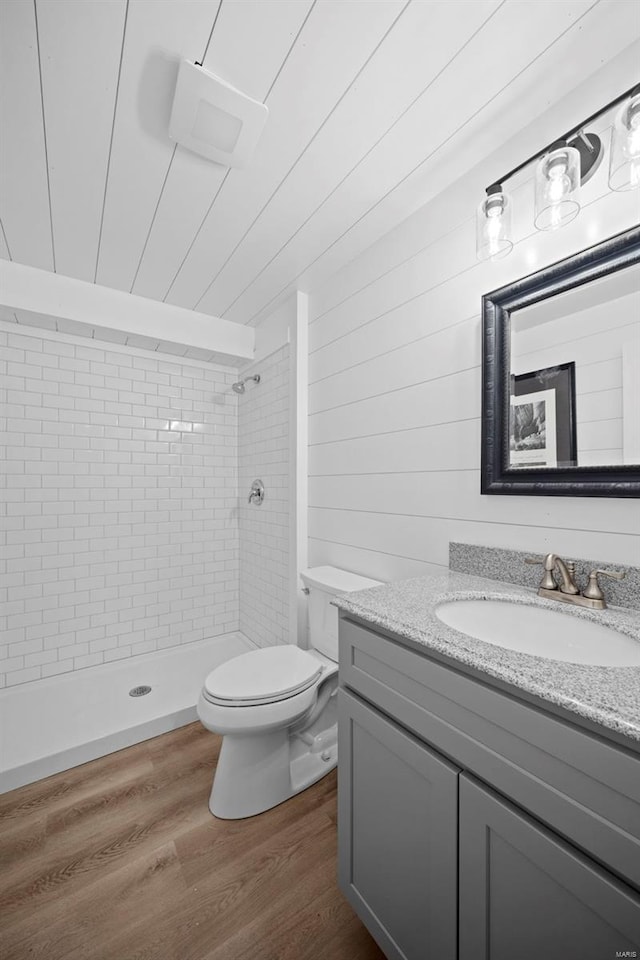 bathroom featuring vanity, a tile shower, toilet, and wood finished floors