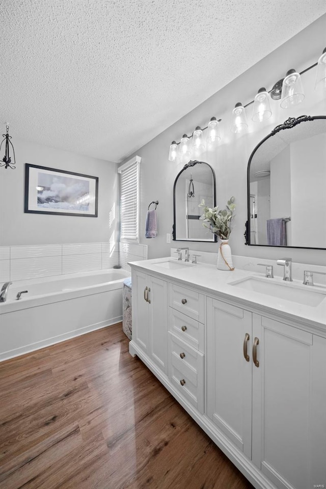 bathroom with double vanity, a textured ceiling, a sink, and wood finished floors