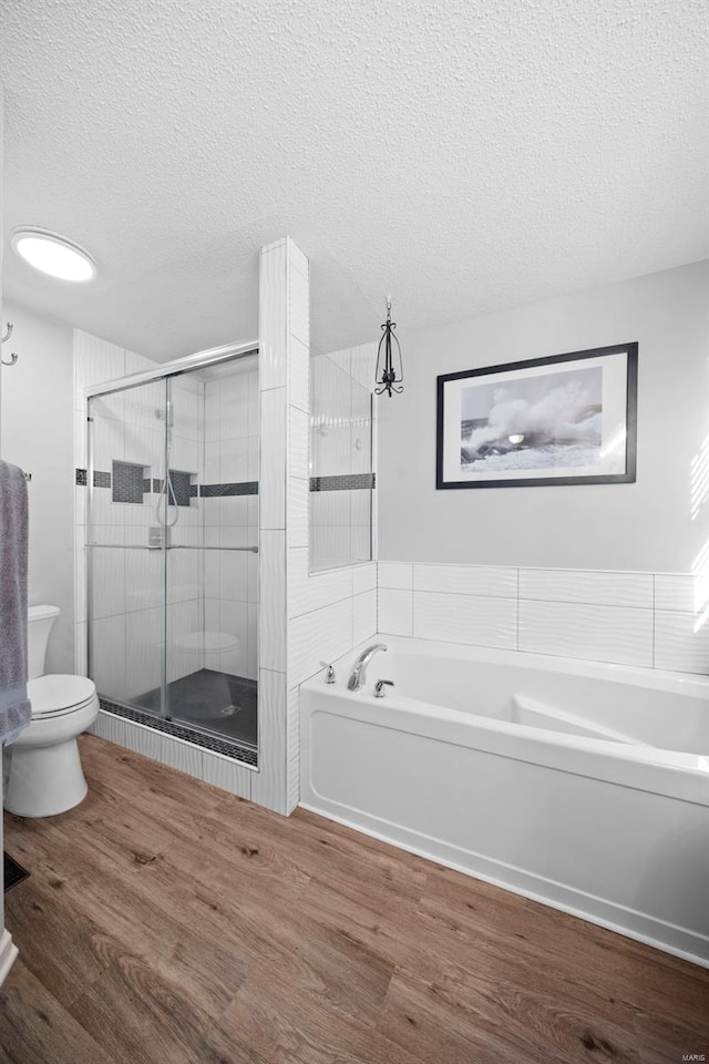 bathroom with toilet, a textured ceiling, a shower stall, wood finished floors, and a bath