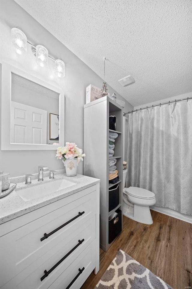 full bathroom with toilet, a textured ceiling, wood finished floors, and vanity