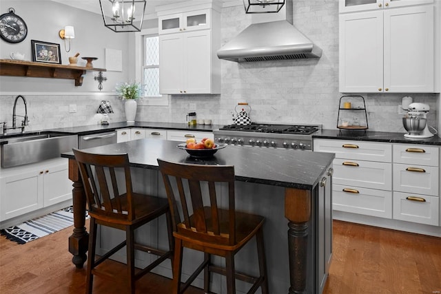 kitchen with wall chimney range hood, a sink, a breakfast bar area, white cabinetry, and backsplash