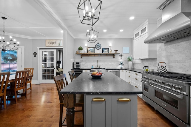 kitchen with open shelves, a sink, an inviting chandelier, stainless steel appliances, and wall chimney exhaust hood