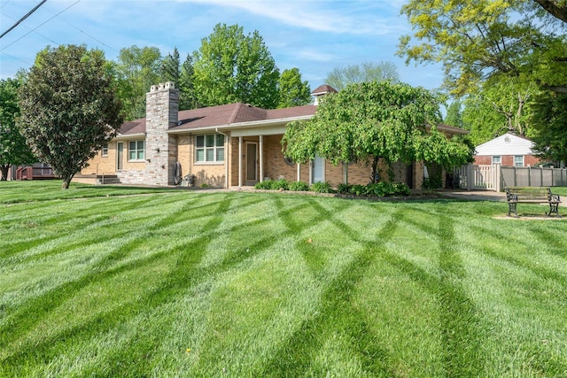 ranch-style home with a chimney, brick siding, a front lawn, and fence