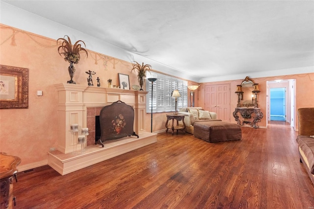 living room with baseboards, wood finished floors, and a fireplace with raised hearth