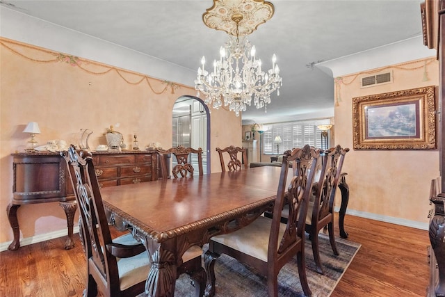 dining room with wood finished floors, visible vents, baseboards, arched walkways, and a chandelier