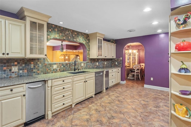 kitchen with stainless steel dishwasher, a sink, arched walkways, tasteful backsplash, and cream cabinets
