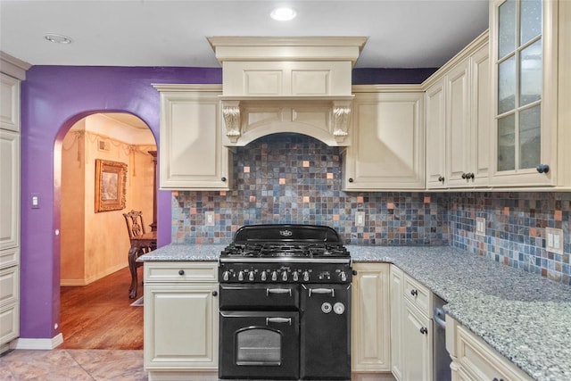 kitchen featuring baseboards, double oven range, light stone counters, arched walkways, and tasteful backsplash