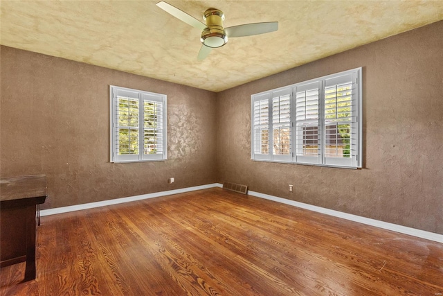 empty room with baseboards, visible vents, ceiling fan, and wood finished floors