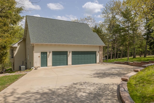 exterior space with roof with shingles, central AC unit, concrete driveway, and an attached garage