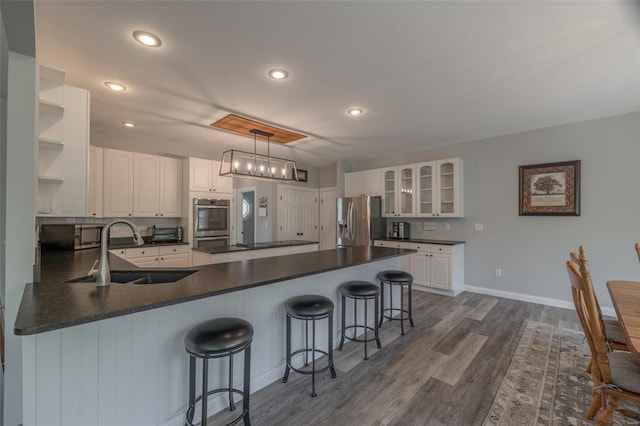 kitchen with a sink, stainless steel fridge, open shelves, a peninsula, and dark countertops