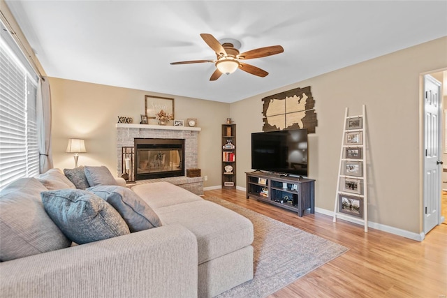 living room with ceiling fan, light wood-style flooring, baseboards, and a glass covered fireplace