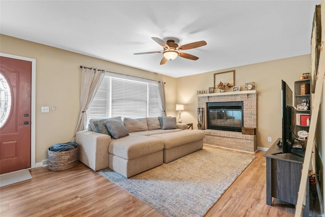 living room with a fireplace, baseboards, a ceiling fan, and light wood-style floors