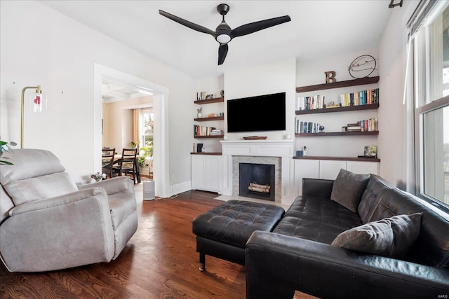living room featuring a fireplace with flush hearth, baseboards, a ceiling fan, and dark wood finished floors
