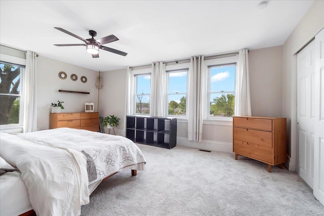 bedroom featuring multiple windows, a closet, ceiling fan, and light colored carpet