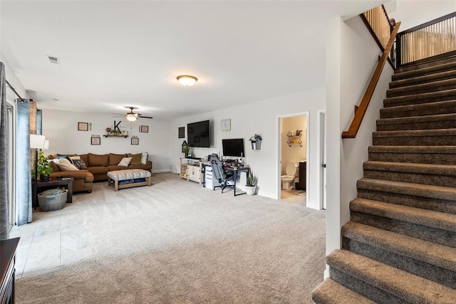 carpeted living area with visible vents, baseboards, ceiling fan, and stairway