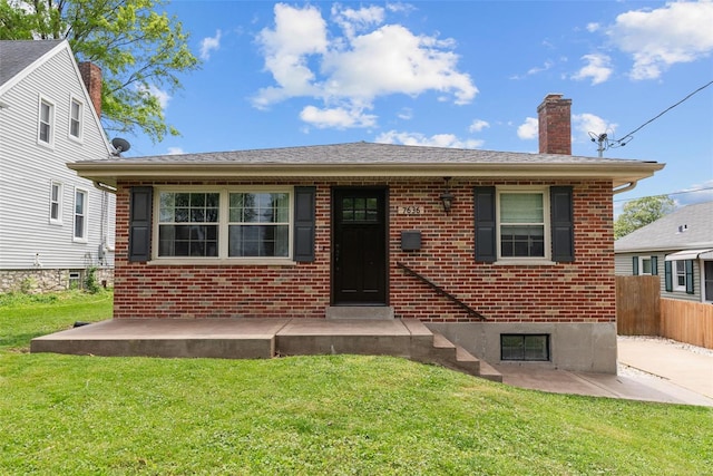 view of front of property featuring fence, a chimney, brick siding, and a front yard