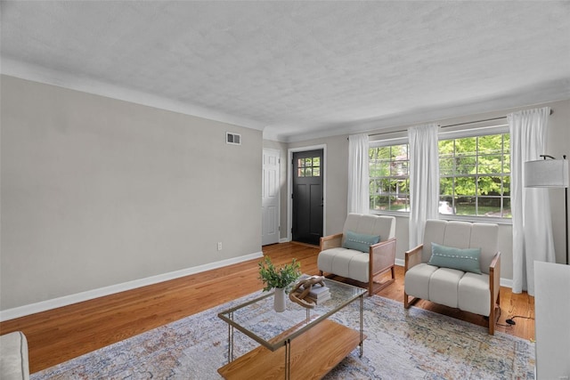 living area featuring baseboards, a textured ceiling, wood finished floors, and visible vents