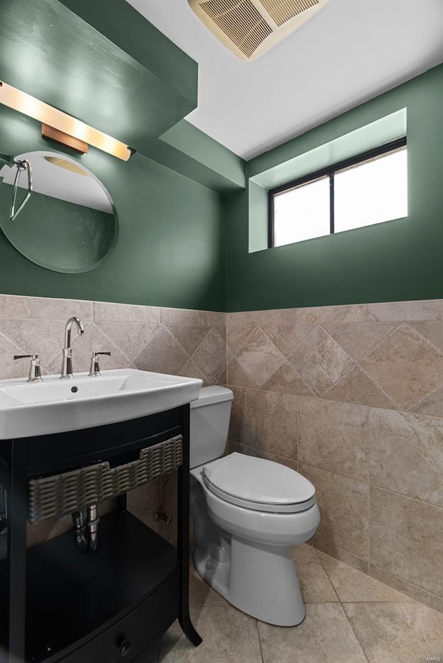 half bathroom featuring tile walls, vanity, toilet, and visible vents