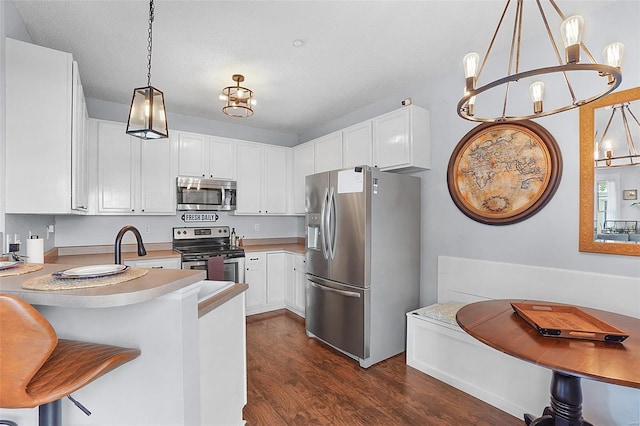 kitchen with a peninsula, dark wood-type flooring, light countertops, appliances with stainless steel finishes, and a notable chandelier