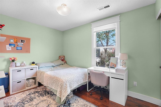 bedroom with baseboards, a textured ceiling, visible vents, and wood finished floors