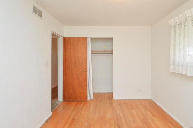unfurnished bedroom featuring baseboards, visible vents, wood finished floors, and a closet