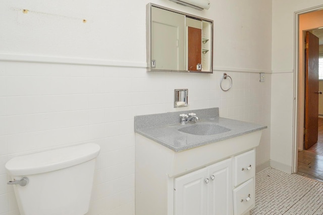 half bathroom with tile walls, a wall mounted air conditioner, a wainscoted wall, vanity, and toilet