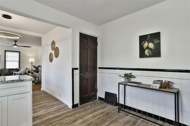 corridor featuring baseboards, wainscoting, wood finished floors, and tile walls