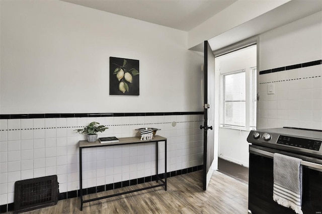 kitchen with tile walls, wainscoting, wood finished floors, and electric stove