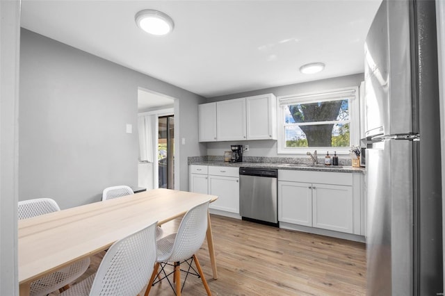 kitchen with stone counters, a sink, white cabinets, light wood-style floors, and stainless steel appliances