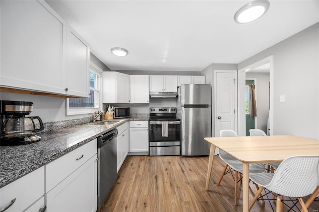 kitchen with a sink, under cabinet range hood, light wood-style floors, stainless steel appliances, and white cabinetry