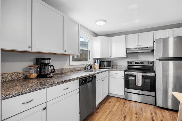 kitchen with appliances with stainless steel finishes, a sink, white cabinets, light wood-style floors, and under cabinet range hood