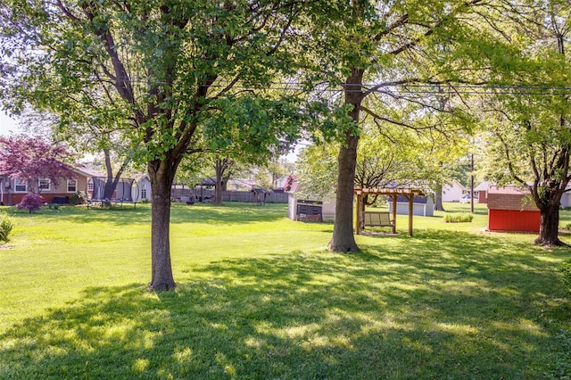 view of yard featuring a trampoline, a storage shed, an outbuilding, fence, and a pergola