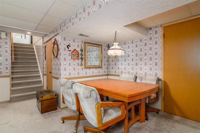 carpeted dining room with stairway, visible vents, wallpapered walls, and a paneled ceiling