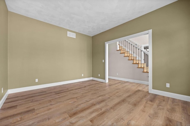 empty room with stairs, baseboards, visible vents, and wood finished floors