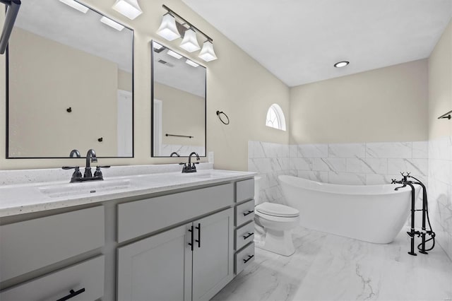 full bathroom with double vanity, a freestanding bath, a sink, and marble finish floor