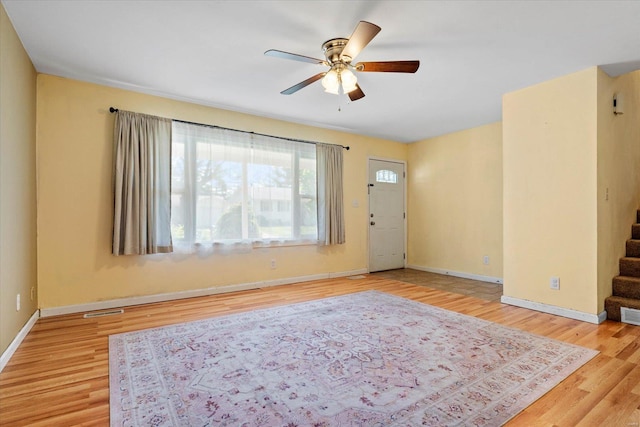 interior space featuring ceiling fan, stairs, baseboards, wood finished floors, and visible vents