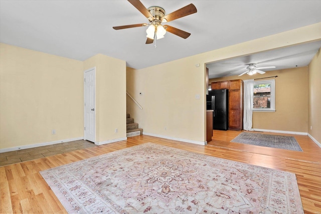 unfurnished living room featuring baseboards, light wood-style flooring, stairs, and ceiling fan