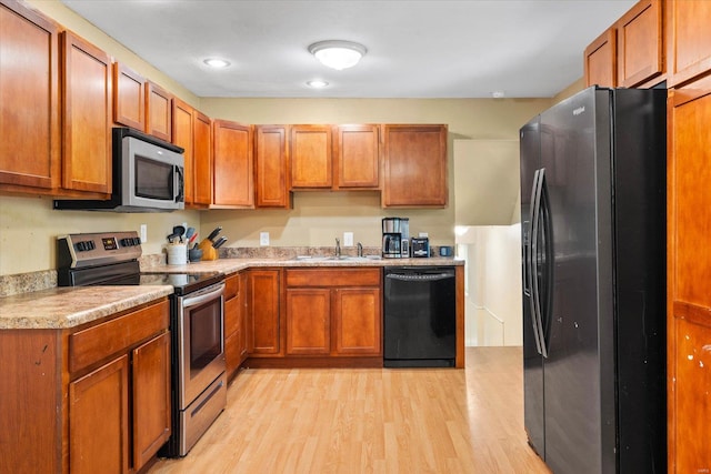 kitchen with light wood-type flooring, light countertops, brown cabinetry, and black appliances