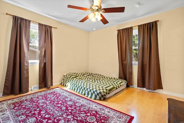 bedroom with baseboards, a ceiling fan, wood finished floors, and visible vents